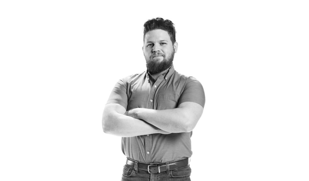 A black & white frontal picture of a man smiling with his arms crossed