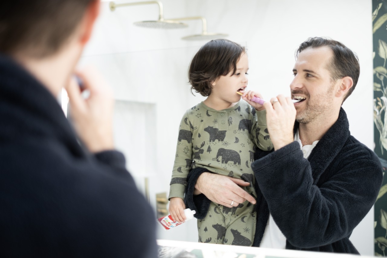 A father and his child brushing their teeth together