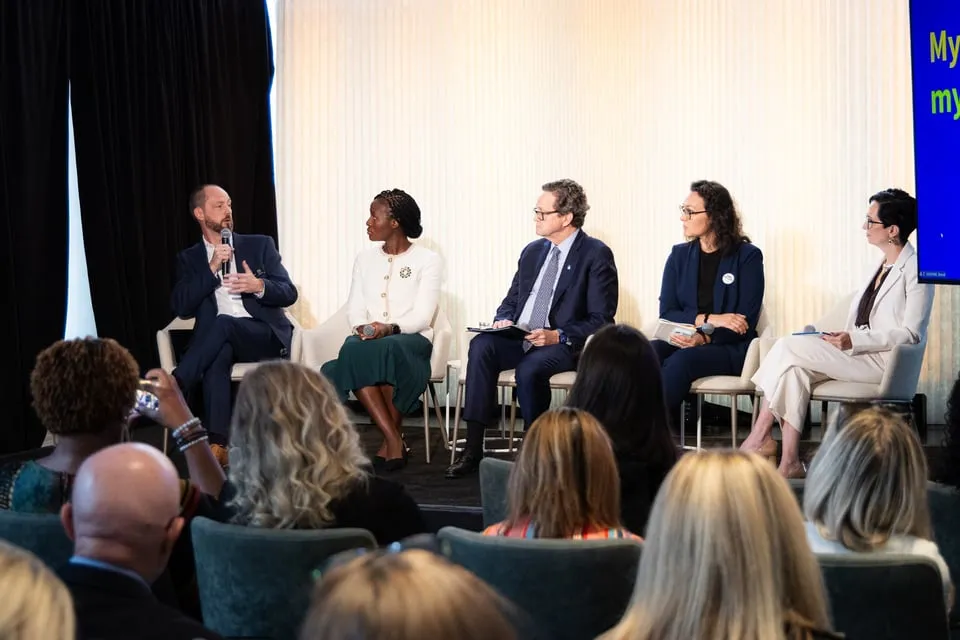 A diverse panel discussing health inequalities and oral health access at an international forum, with audience members listening