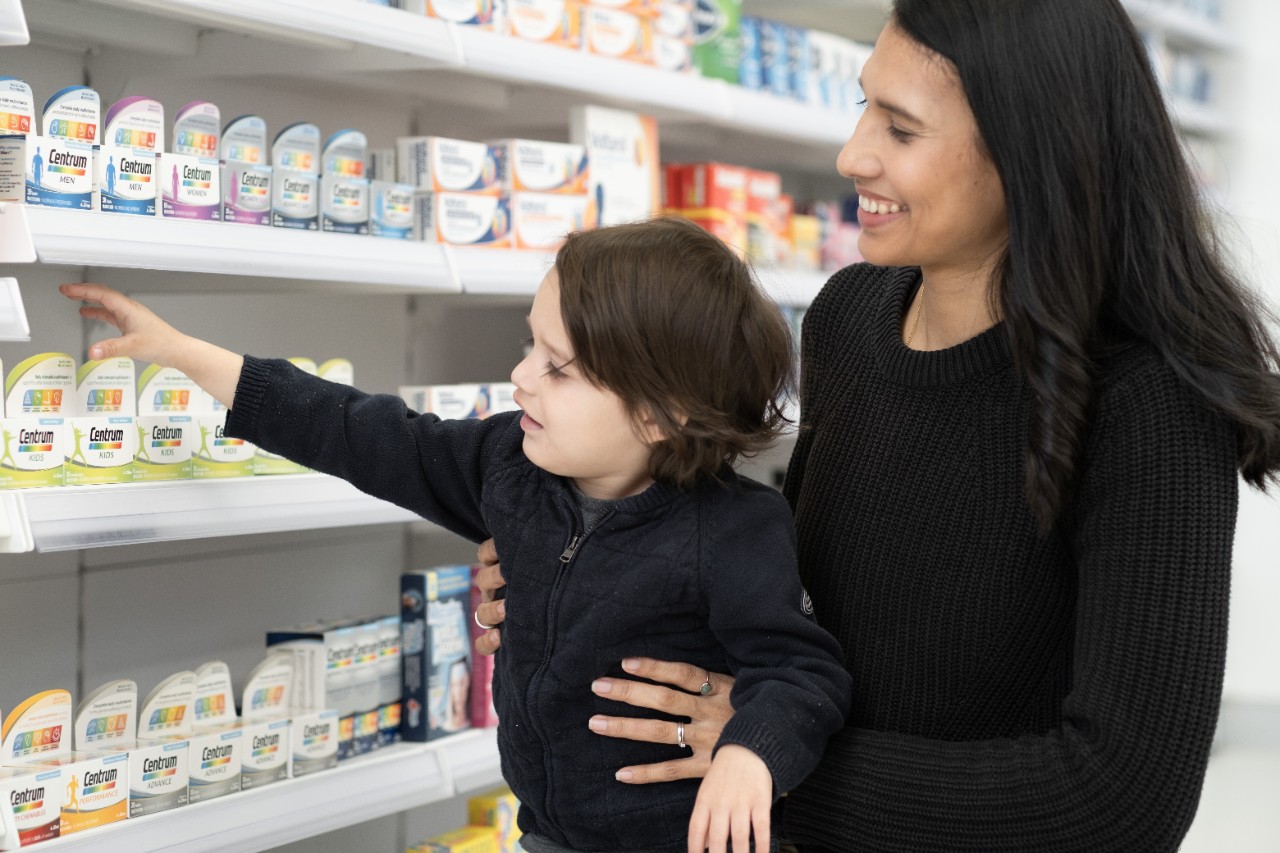 Mother and child shopping in store, reaching for Centrum product on aisle shelf