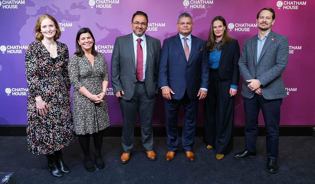 Group of people standing in front of a branded Chatham House backdrop at an indoor event, dressed in business attire and facing the camera