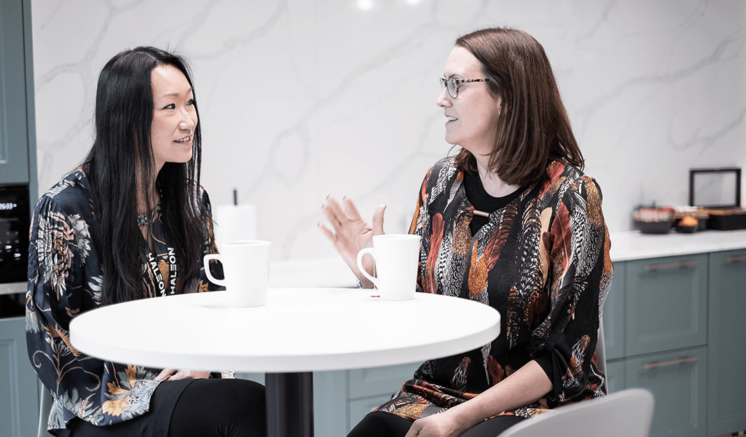 Two women seated at a small white round table, discussing over a cup of coffee