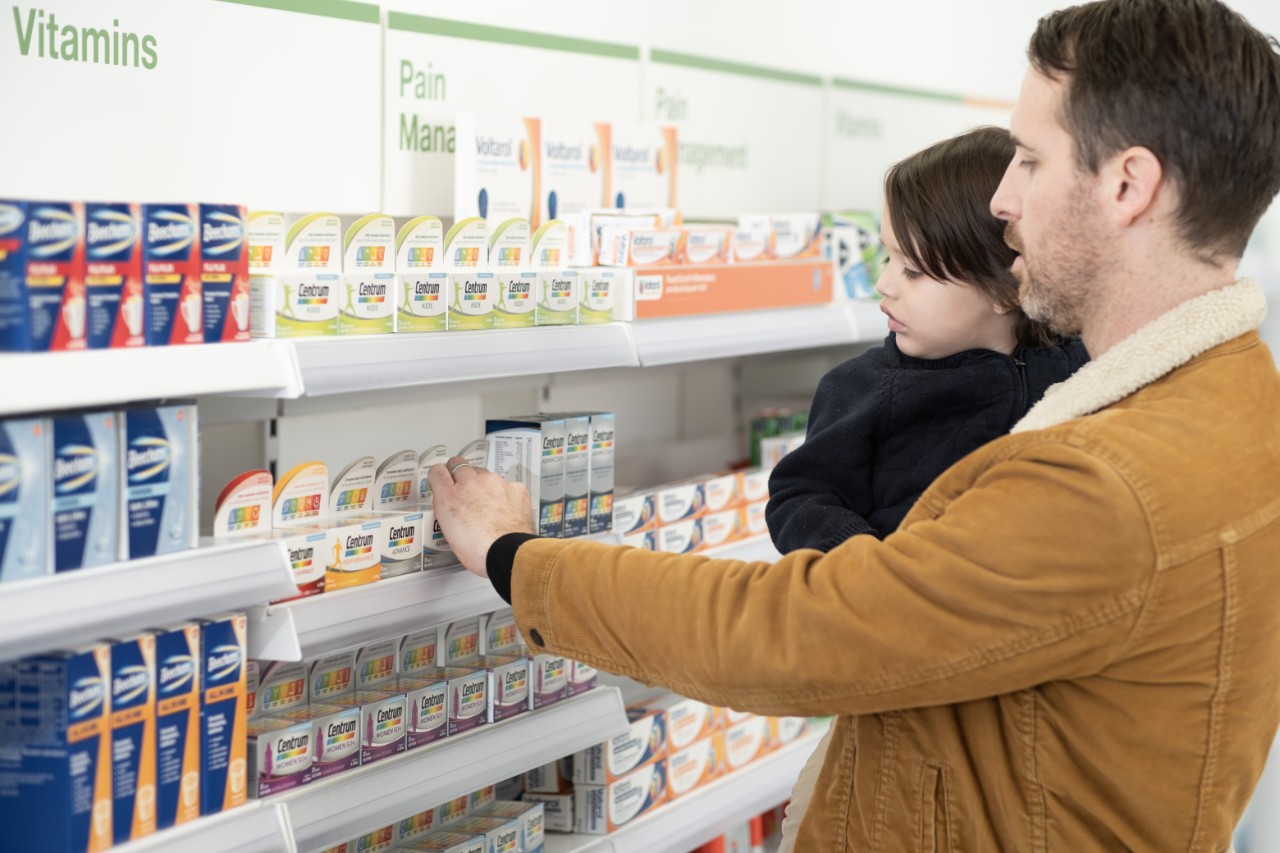 Father and child shopping in store, reaching for Centrum product on aisle shelf.