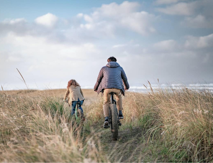 Father and daughter cycling in a field, viewed from behind