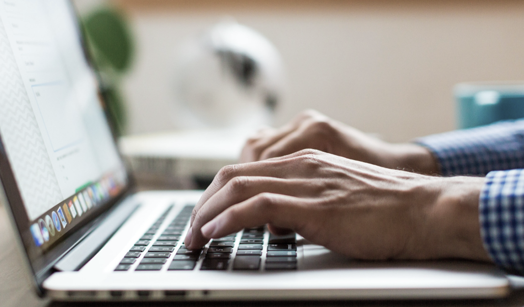  Side view close-up of hands typing on a Mac laptop keyboard