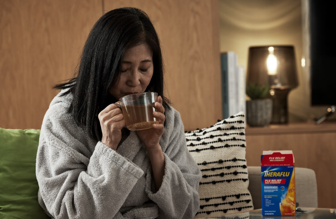 Woman in robe drinking Theraflu