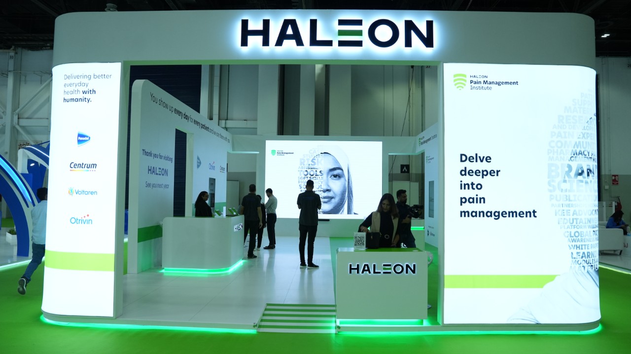 Haleon exhibition stand at an indoor event, featuring illuminated branding, information panels, and people standing within the booth.
