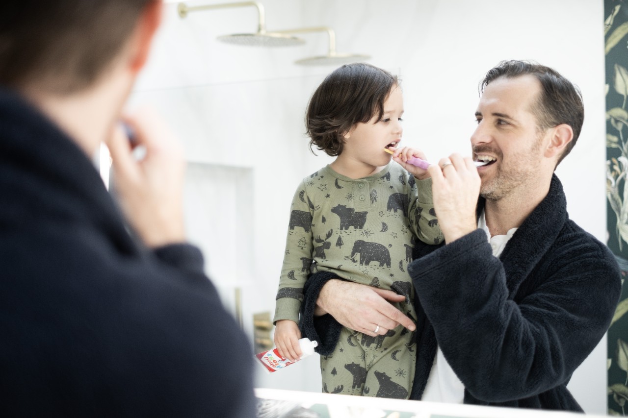 A father and his child brushing their teeth together