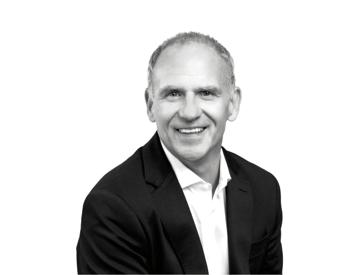 A headshot of a person smiling at the camera, the image is in black and white  	 	