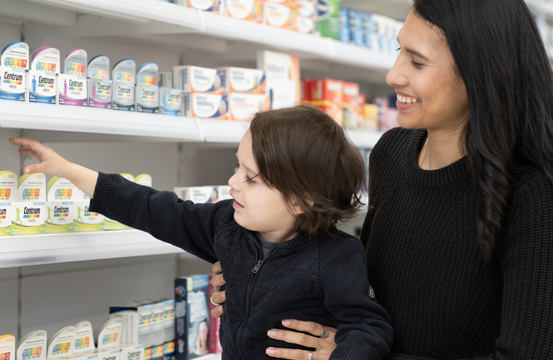 Mother and child shopping in store, reaching for Centrum product on aisle shelf